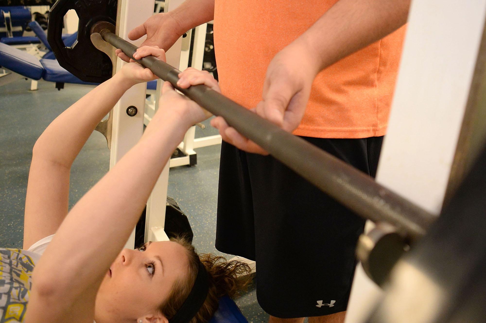 A student spotting another student lifting weights